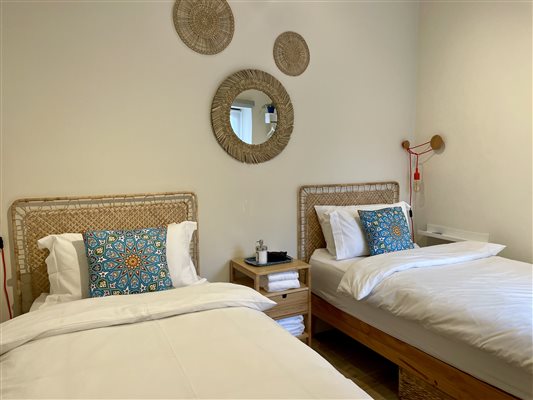 Twin Beds with white bed linen, and bright blue cushions. On the wall is a round mirror.  